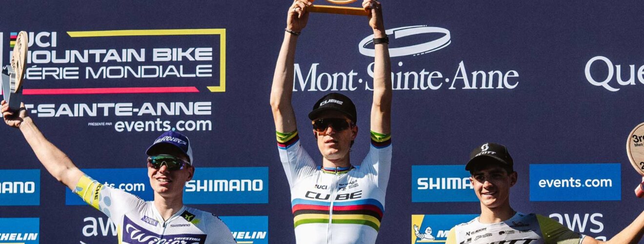Finn Treudler célèbre la finale de la saison du Cube Factory Racing 2025 à Mont-Sainte-Anne, tenant le trophée dans ses mains, entouré des deuxième et troisième coureurs sur le podium.