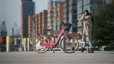 Une femme court dans une ville vers un vélo électrique rose Cube Ella Hybrid.