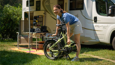 Une femme se tient devant un camping-car, devant elle se trouve un vélo pliable vert.