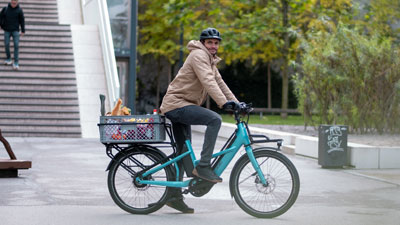 Un cycliste traverse le centre-ville sur son vélo bleu Cube Longtail. Il transporte une caisse de provisions sur son porte-bagages.
