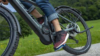 La photo montre un gros plan d'un vélo hybride tout-terrain gris Cube Reaction. On voit en détail le pédalier et le bloc moteur du vélo électrique pendant la conduite.