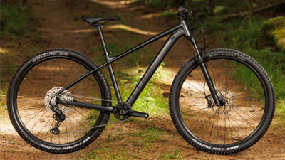 On voit un VTT Cube noir posé sur un chemin forestier.