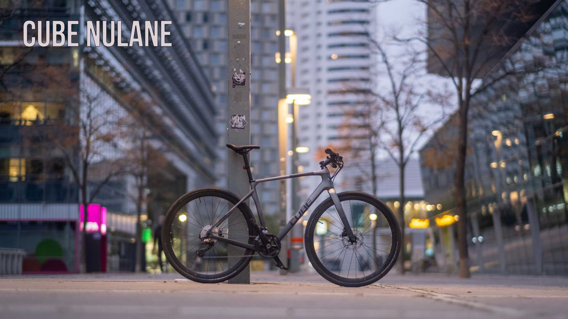 Bannière portant l'inscription Cube Nulane . Un vélo d'appartement Cube Nulane est appuyé contre un pilier dans le centre-ville.