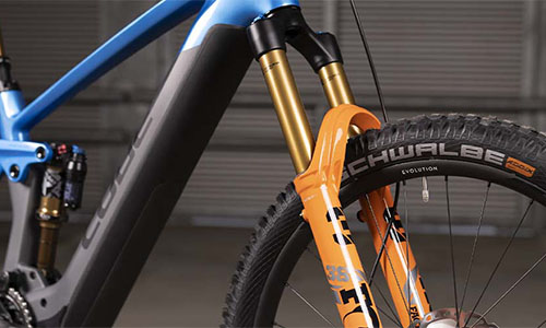 On voit un vélo bleu avec un gros plan sur la suspension de la fourche.