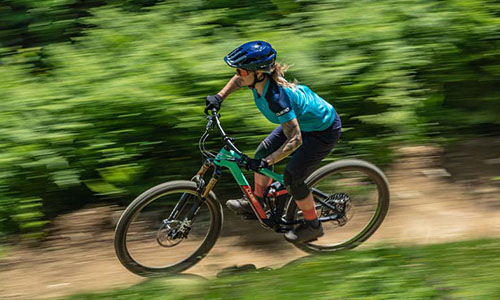 On voit une femme sur un VTT qui roule rapidement sur un chemin forestier.