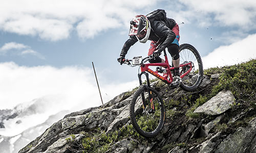 Un cycliste de descente avec un casque intégral descend une montagne rocailleuse.