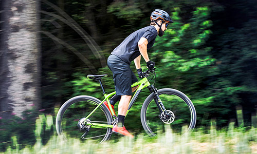 Cycliste roulant debout sur un VTT hardtail vert dans un environnement naturel verdoyant.