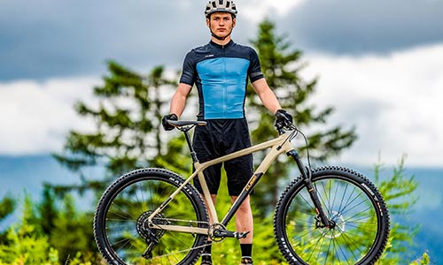 Un Homme en tenue de cycliste debout derrière un VTT semi-rigide.