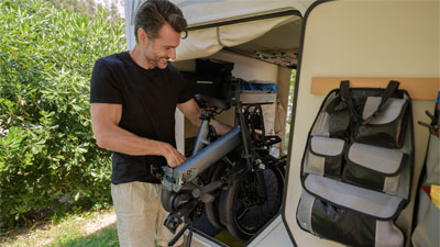 Un homme range son vélo pliant gris dans son camping-car ouvert.