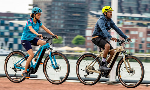 Un homme et une femme roulent sur une piste cyclable, avec une grande ville en arrière-plan.