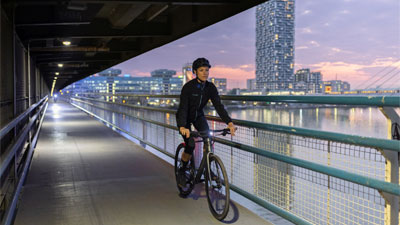 On voit une femme à vélo qui traverse un passage souterrain, avec une grande ville en arrière-plan.