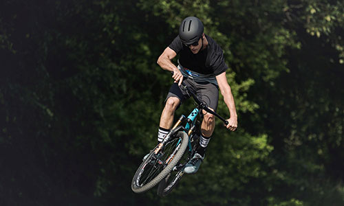 Un cycliste saute avec une moto tout-terrain bleu clair, avec des arbres en arrière-plan.