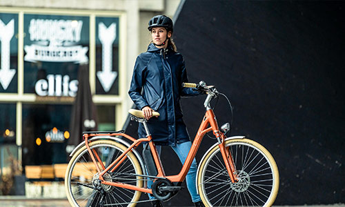 Une femme se tient derrière son vélo orange, dans le centre-ville.